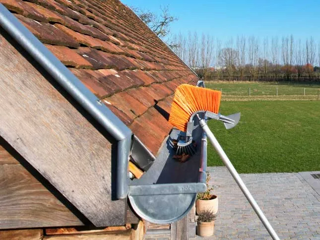 Dakgoot wordt met een borstel vanaf veilige afstand gereinigd